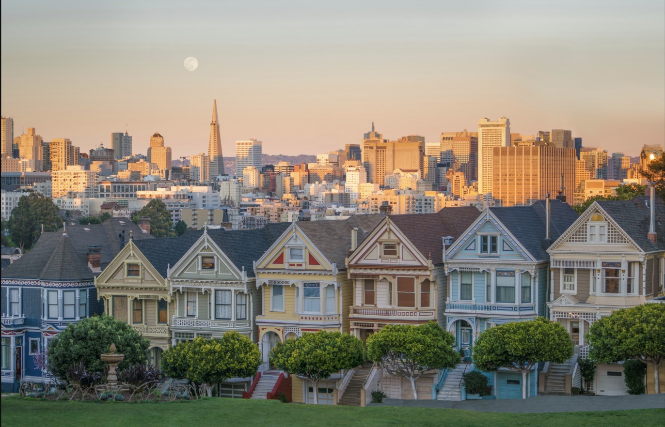 Row of Victorian houses in San Francisco with the downtown skyline behind them